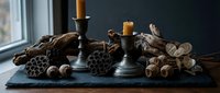 Autumn table centerpiece with pinecones, walnuts and candles on dark slate board creating cozy seasonal home decor atmosphere for fall celebrations.