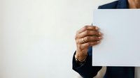 Businessman holding blank white card or paper in hand against neutral background for corporate messaging and branding purposes.