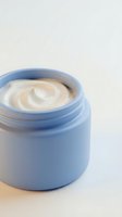 Open blue jar with creamy beige moisturizer or skincare product inside, isolated on white background for cosmetics, beauty, and wellness design projects.