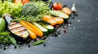 Fresh grilled vegetables and herbs arranged on dark stone background with salt and peppercorns, colorful healthy ingredients for cooking.