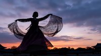 Woman dancing with flowing fabric against dramatic sunset sky creating elegant silhouette for artistic and lifestyle concepts.