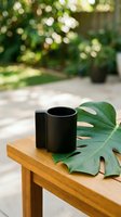 Black ceramic mug on wooden table with tropical monstera leaf in natural garden setting with soft bokeh background for lifestyle branding.