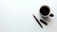 Minimalist workspace with black coffee cup, fountain pen and cap on clean white background for business and productivity concepts.