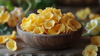 Raw yellow pasta shells in rustic wooden bowl on dark table, scattered pieces create natural composition with soft lighting and blurred background.