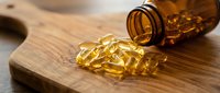 Golden omega-3 fish oil capsules spilling from amber glass bottle onto wooden surface for health and wellness supplement nutrition concept.