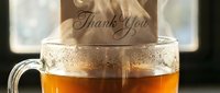Steaming glass mug of hot tea with a thank you card tucked inside, warm and cozy atmosphere, gratitude concept for greeting cards.