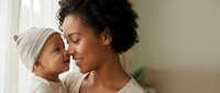 Young African American mother holding baby in tender moment by window with natural light creating warm intimate family bonding scene for parenting content.
