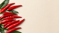 Fresh red hot chili peppers with green leaves arranged on beige background, copy space for text. Natural food photography layout for spicy cuisine.