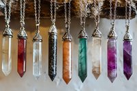 Crystal point pendants in various colors including amethyst, quartz, fluorite and carnelian on silver chains against natural wooden background for jewelry design.