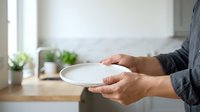 Close-up of male hands holding empty white plate in modern kitchen with natural light, suitable for food service, restaurant, dining and culinary content.