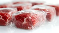 Fresh raw beef chunks individually vacuum sealed in clear plastic wrap with selective focus showing marbled meat texture and preservation method.
