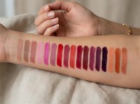 Colorful lipstick swatches on woman's arm showing makeup palette range from nude to bold shades for beauty testing and cosmetic product selection.