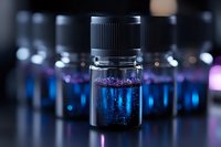 Glass vial with glowing blue liquid and particles against dark background with multiple blurred vials, creating mysterious laboratory atmosphere.