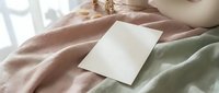 Blank white card mockup on soft pastel bedding with natural sunlight creating gentle shadows for branding and stationery design projects.