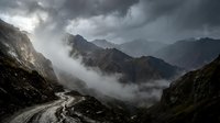 Dramatic mountain landscape with winding road through misty peaks and stormy clouds creating moody atmospheric scenery for travel and adventure themes.