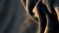 Close-up of textured fabric with warm golden light casting dramatic shadows across woven material, suitable for backgrounds and design projects.
