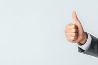 Businessman in formal suit showing thumbs up gesture against light background, positive feedback and approval concept for business presentations.