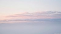 Soft pastel sky at sunrise with gentle pink and lavender clouds above a misty horizon, evoking calm and serenity.