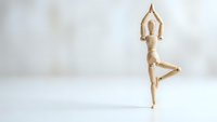 Wooden mannequin performing tree yoga pose on white surface against neutral background for wellness and mindfulness concepts.
