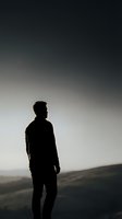 Silhouette of young man standing against dramatic gradient sky at dusk, contemplative mood for mental health and personal growth concepts.
