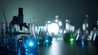Modern laboratory with microscope and glowing blue chemical solutions in glass beakers creating atmospheric scientific research environment.