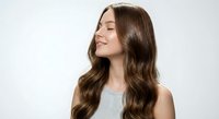 Young brunette woman with long wavy hair smiling peacefully with eyes closed against white background for beauty and wellness campaigns.