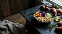 Healthy Buddha bowl with chickpeas, roasted vegetables, and fresh greens on dark slate surface. Nutritious meal prep concept for wellness lifestyle.
