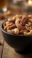 Mixed nuts with sea salt in black bowl on rustic wooden table with warm lighting for healthy snacking and cooking ingredients.
