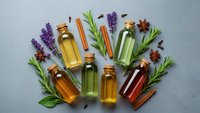 Essential oils in glass bottles with fresh herbs lavender rosemary cinnamon sticks and star anise arranged on textured surface for aromatherapy wellness spa treatments.