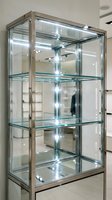 Modern glass display cabinet with LED lighting and chrome frame for retail store merchandise presentation in commercial interior space.