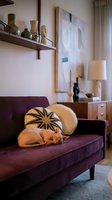 Cozy living room interior with burgundy velvet sofa, decorative pillows, wooden shelf with vases, abstract artwork, table lamp, and warm ambient lighting for home decor and interior design projects.