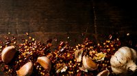 Garlic cloves and whole bulbs scattered on dark rustic wooden surface with warm lighting, suitable for food photography, culinary blogs, recipe websites, and cooking-related content.