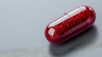 Red glittery capsule pill on gray background with soft shadow, pharmaceutical and medical concept showing medicine and drug development innovation.