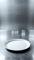 Empty white plate on textured metal surface with blurred industrial background, suitable for food styling, restaurant menus, culinary presentations, and dining concepts.
