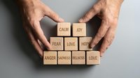 Hands arranging wooden blocks with emotion words calm joy fear love hope anger sadness forming a pyramid concept of mental health balance.