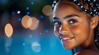 Young African American woman with braided hairstyle and glowing skin smiling against blurred bokeh lights background creating magical evening atmosphere.