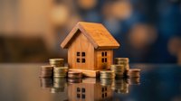 Wooden house model surrounded by stacked coins on reflective surface representing real estate investment, mortgage savings, property financing concept.