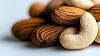 Mixed raw almonds and cashews on white background, macro close-up showing detailed nut texture and natural patterns. Fresh healthy snack composition.