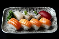 Fresh nigiri sushi assortment with salmon, white fish and tuna served on traditional Japanese ceramic plate against dark background. Asian cuisine delicacy.
