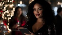 Woman with dark wavy hair and medium skin tone wearing sparkly black outfit at festive evening event with golden bokeh lights and blurred guests in background.