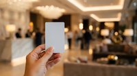 Closeup of hand holding blank white card in luxury hotel lobby with blurred guests and elegant interior design in background.