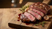 Grilled beef steak sliced on wooden cutting board with herbs and red wine sauce, perfect for restaurant menus and culinary presentations.