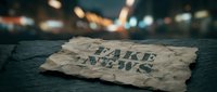 Crumpled fake news newspaper headline lies on dark pavement with blurred city lights background, representing media misinformation and propaganda concepts.