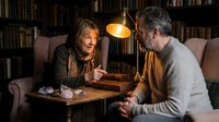 Senior couple enjoying intimate conversation in cozy library setting with warm lighting and bookshelves for lifestyle and relationship content.