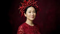 Asian woman wearing sparkly red garment with decorative red spiky headpiece against dark burgundy background. Suitable for holiday campaigns, festive celebrations, fashion editorials, and seasonal marketing materials.