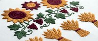 Colorful embroidered sunflowers and grapes on white fabric with decorative stitching patterns for textile design and craft projects.