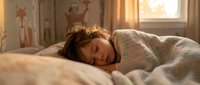 Young woman peacefully sleeping in cozy bedroom with warm morning sunlight streaming through window, comfortable bedding and relaxed atmosphere.