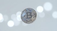 Silver bitcoin cryptocurrency coin floating against soft gray background with elegant bokeh light effects for financial technology concepts.
