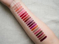 Colorful lipstick swatches on woman arm showing various shades from pink to burgundy for makeup testing and beauty product comparison.