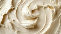 Creamy vanilla frosting swirls in smooth textured waves creating luxurious dessert background pattern. Soft ivory buttercream close-up shows rich culinary detail.